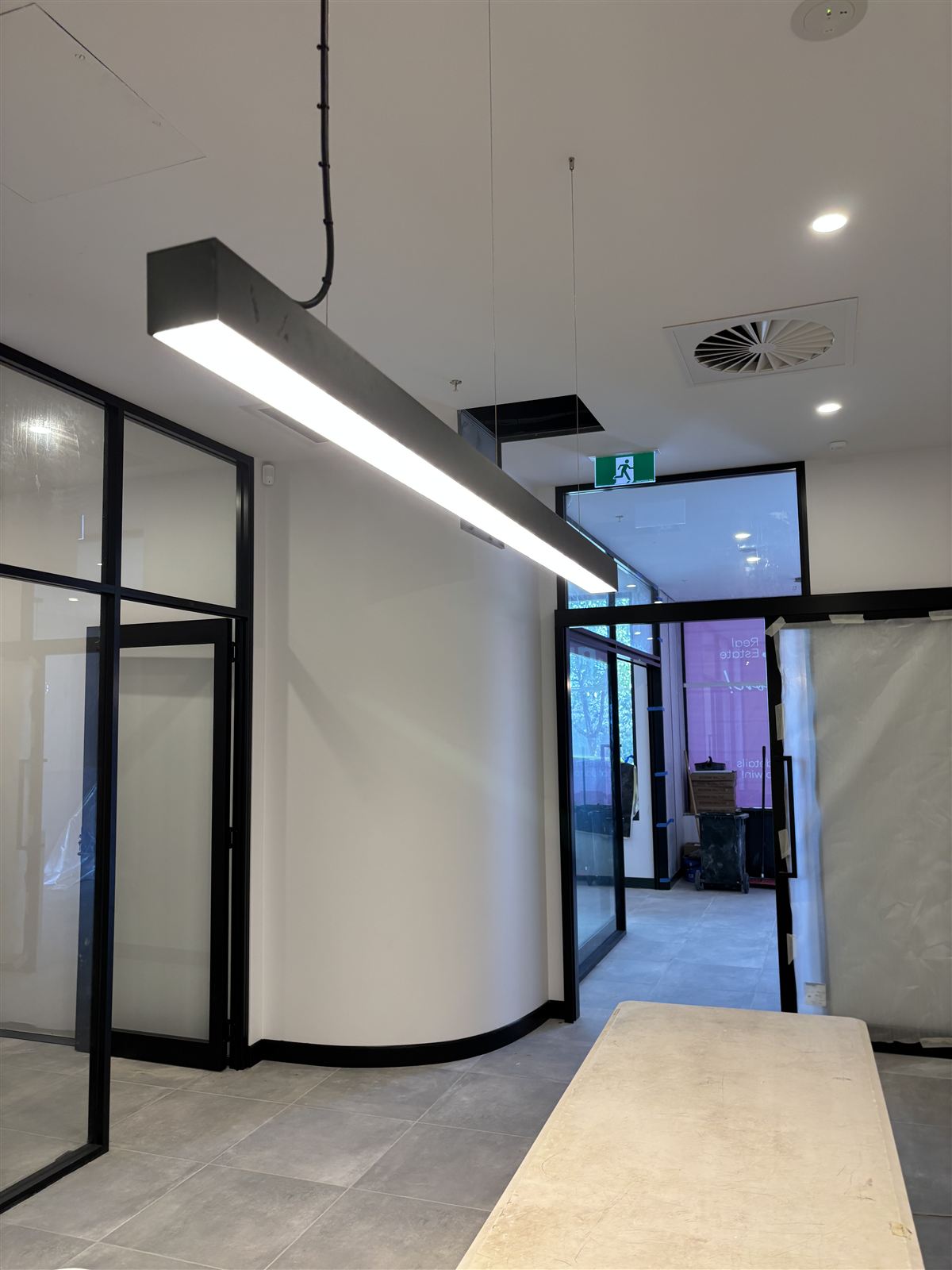 Commercial fit-out with a linear LED pendant, glass partitions and a lit exit sign
